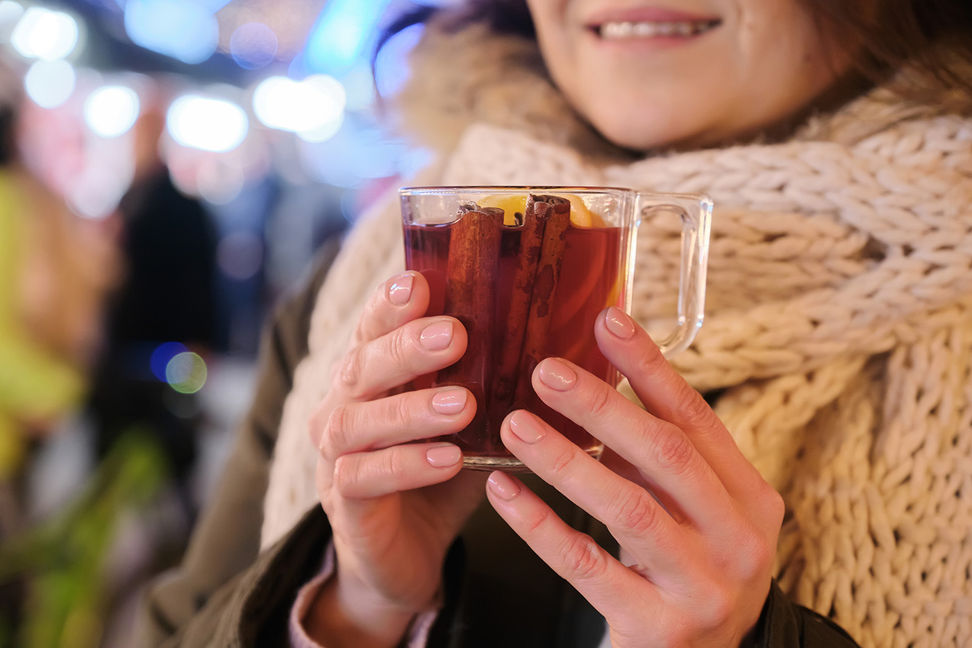 Close-up mug with mulled wine in woman hands, outdoor christmas evening market background